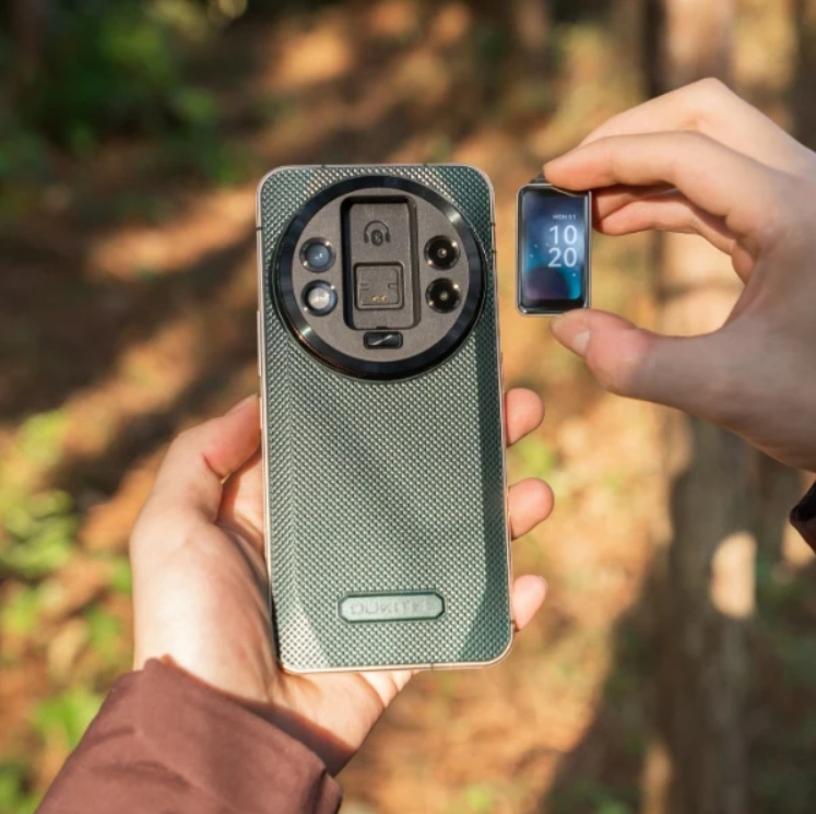 Person holding a smartphone with a large camera lens and a small device displaying numbers outdoors.